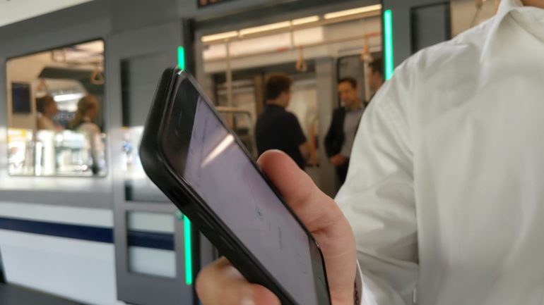 Hand holding a mobile phone in front of a tram